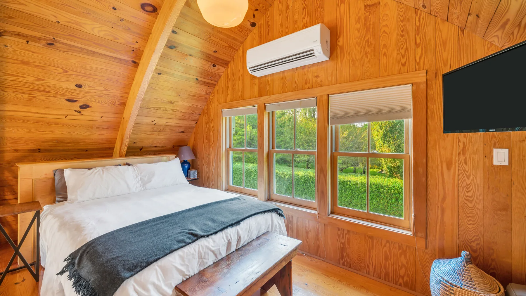 Dormitorio con una cama junto a paredes revestidas de madera y ventanas.