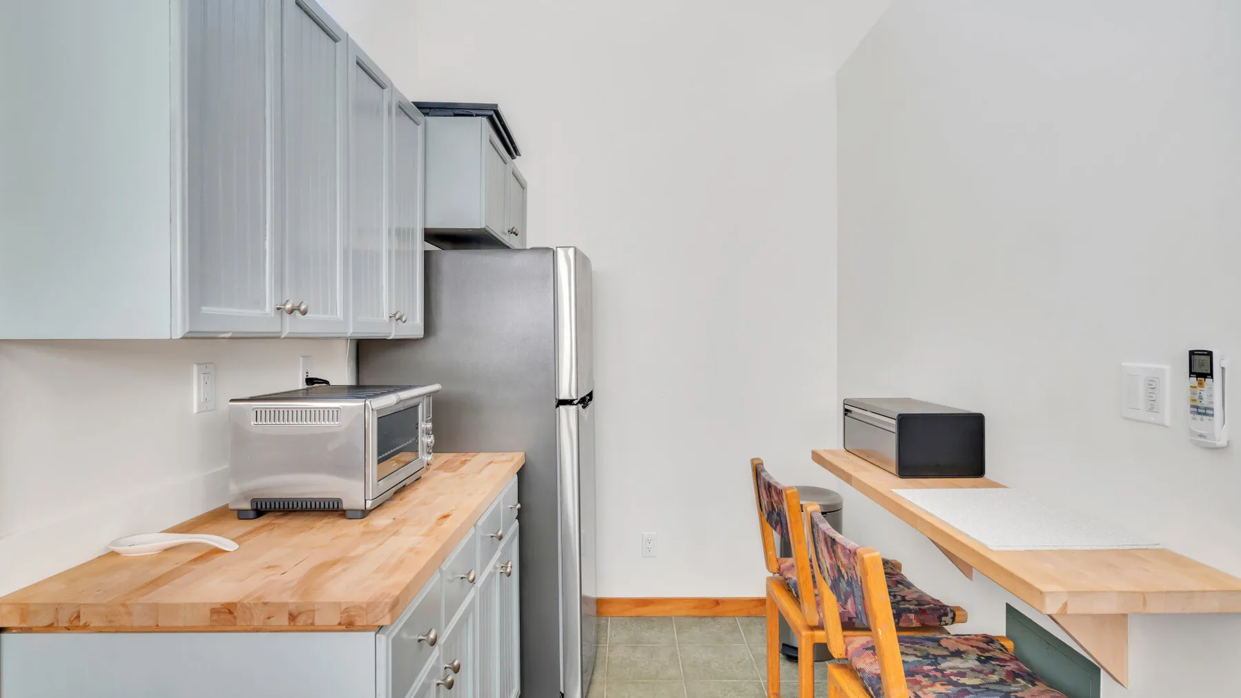 Una cocina luminosa con gabinetes claros, una encimera de madera y un refrigerador.