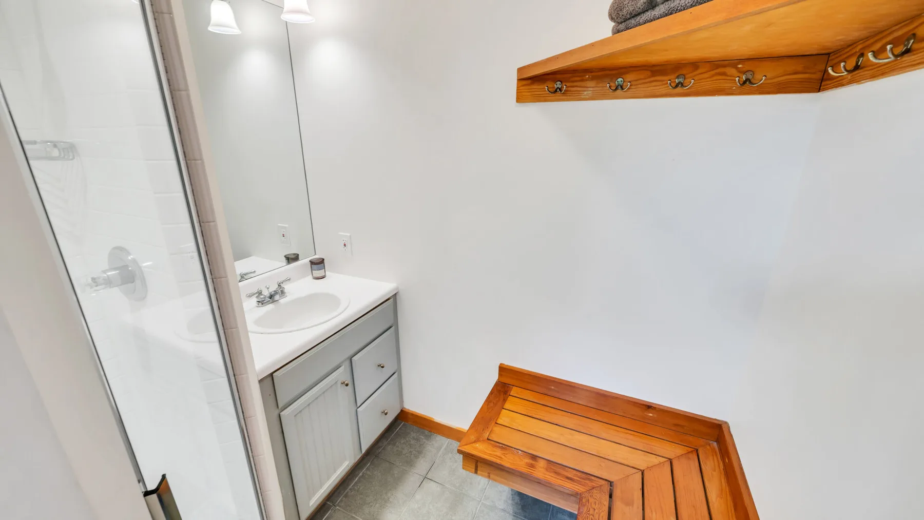 Un baño luminoso con ducha de vidrio, lavabo y banco de madera.
