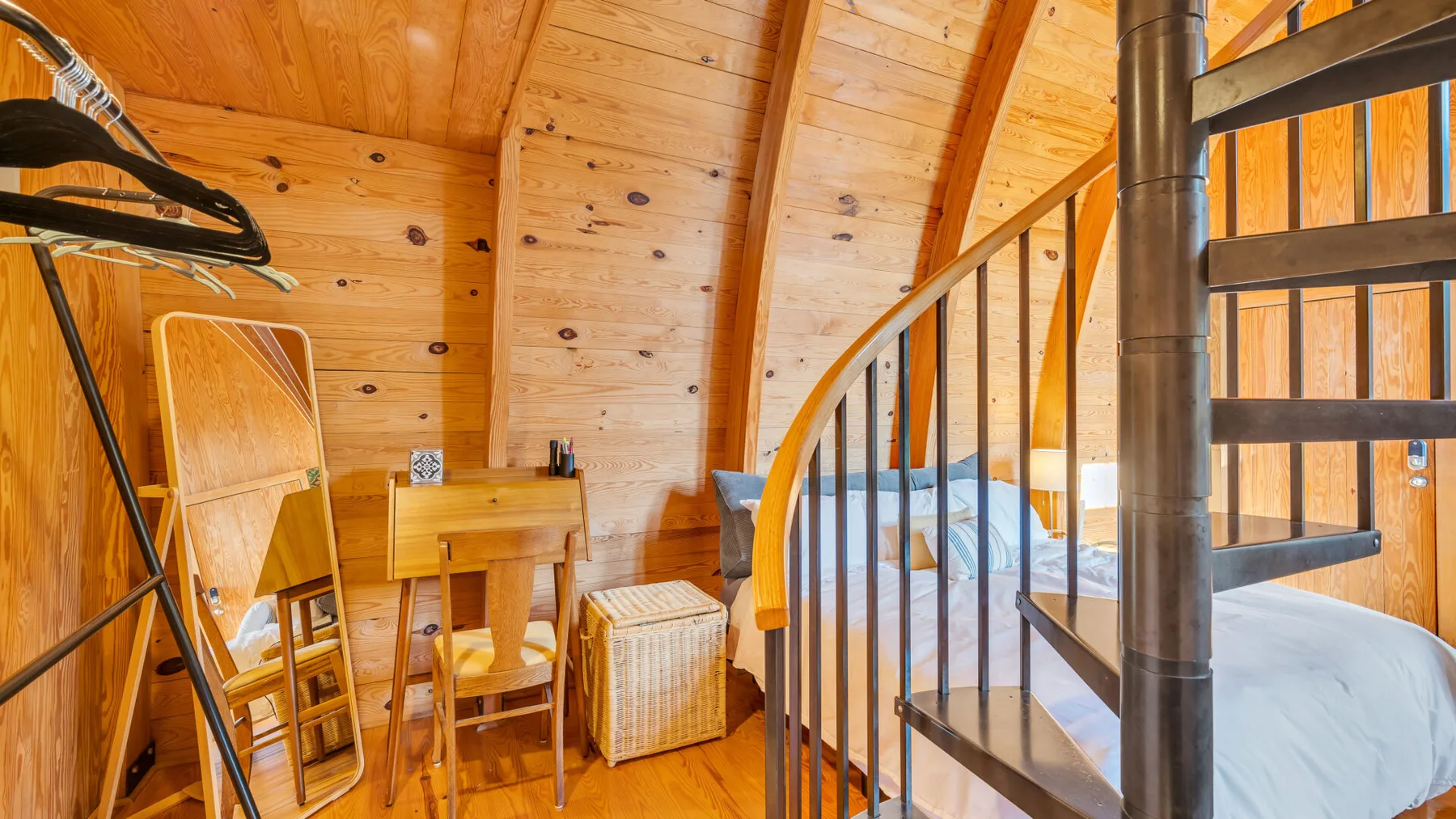 Una zona para dormir revestida de madera tiene una cama junto a una mesa pequeña y sillas.