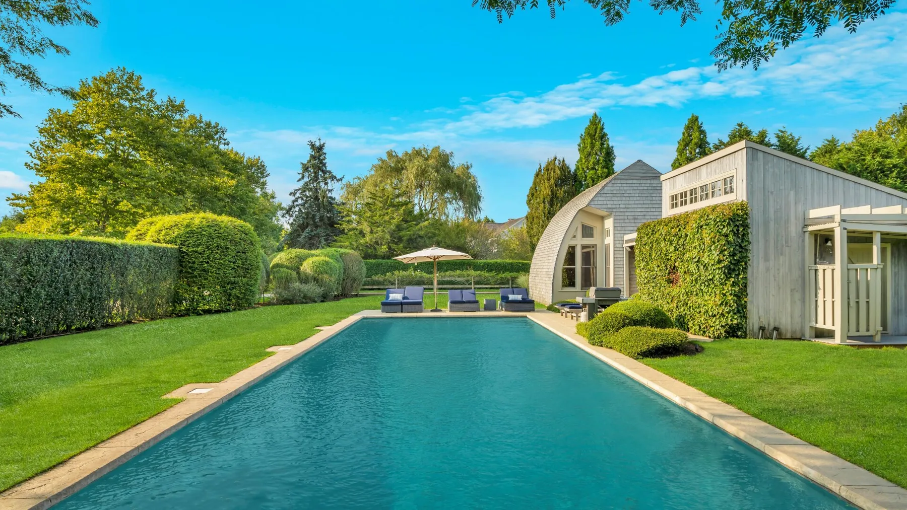 Una piscina al aire libre junto a un edificio moderno y un jardín cuidado.
