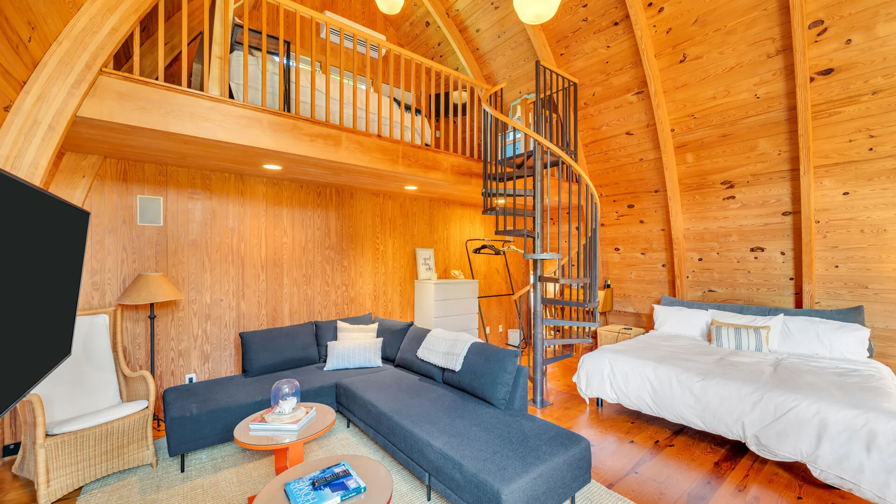 Una sala con revestimiento de madera y zona de descanso con un sofá seccional y una cama.
