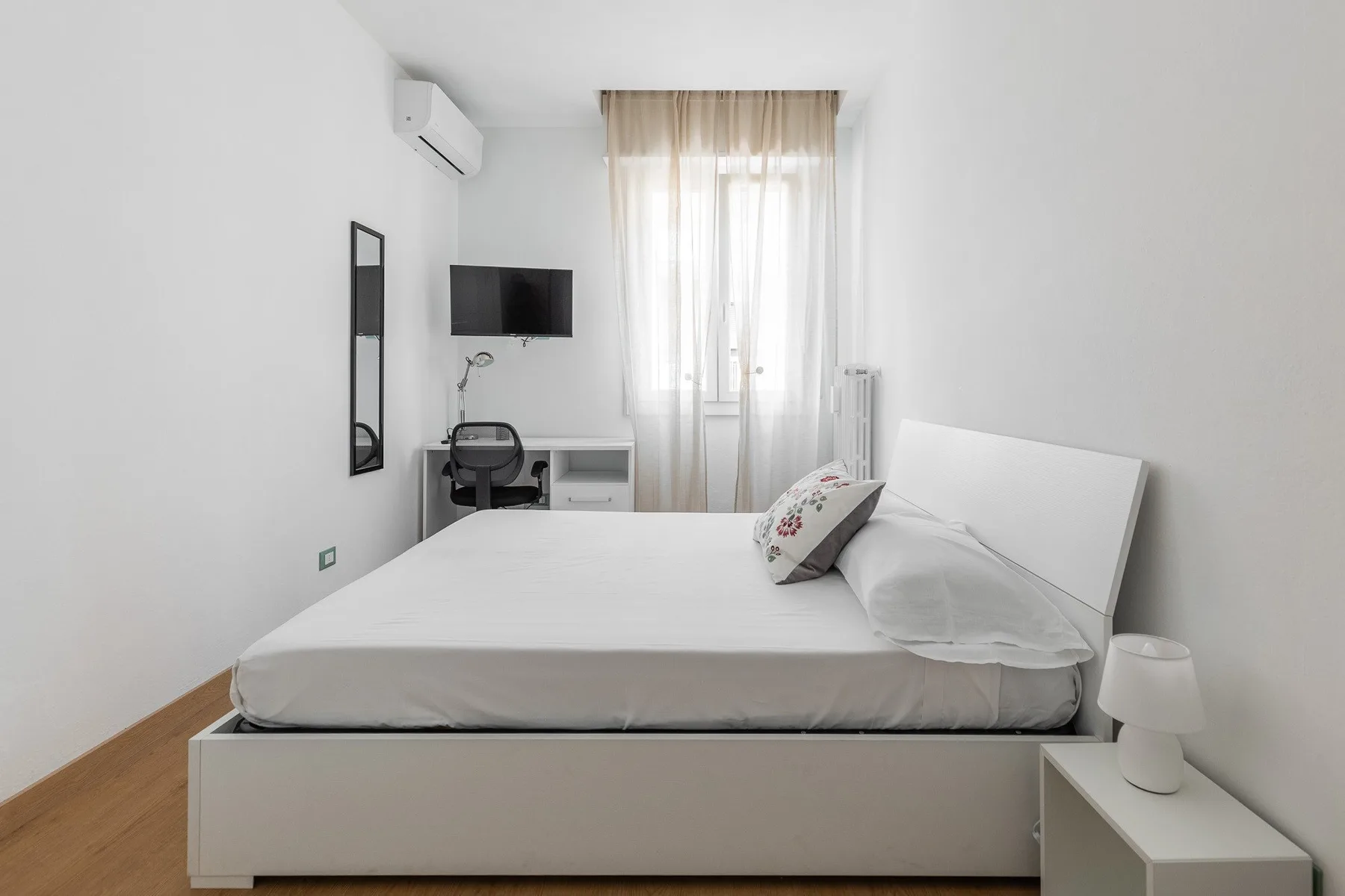 Un dormitorio luminoso con una cama, un escritorio y una ventana.