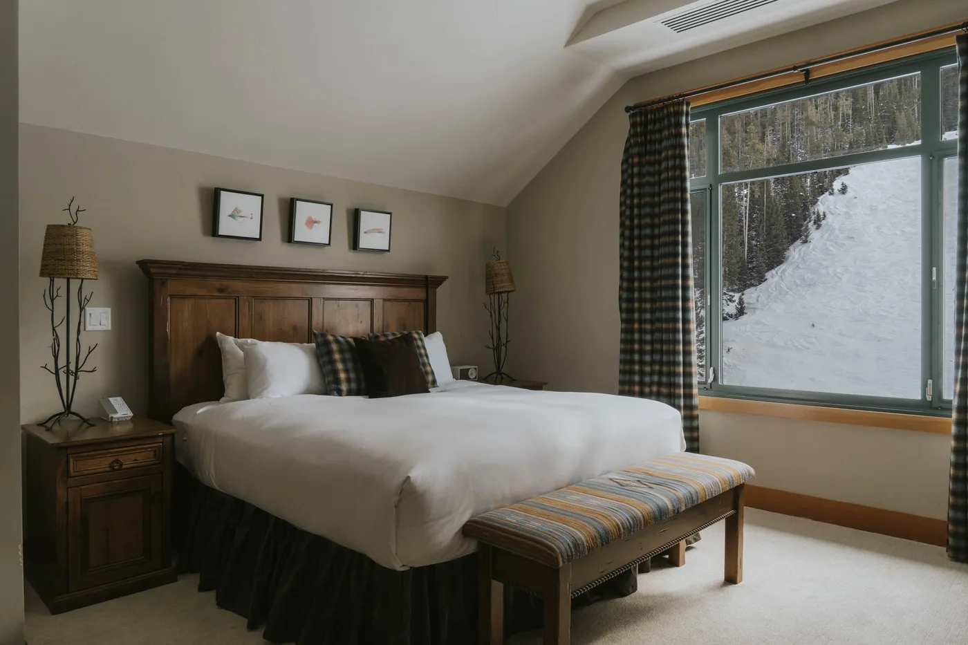 A bedroom with a large bed, a bench, and a window overlooking snow.