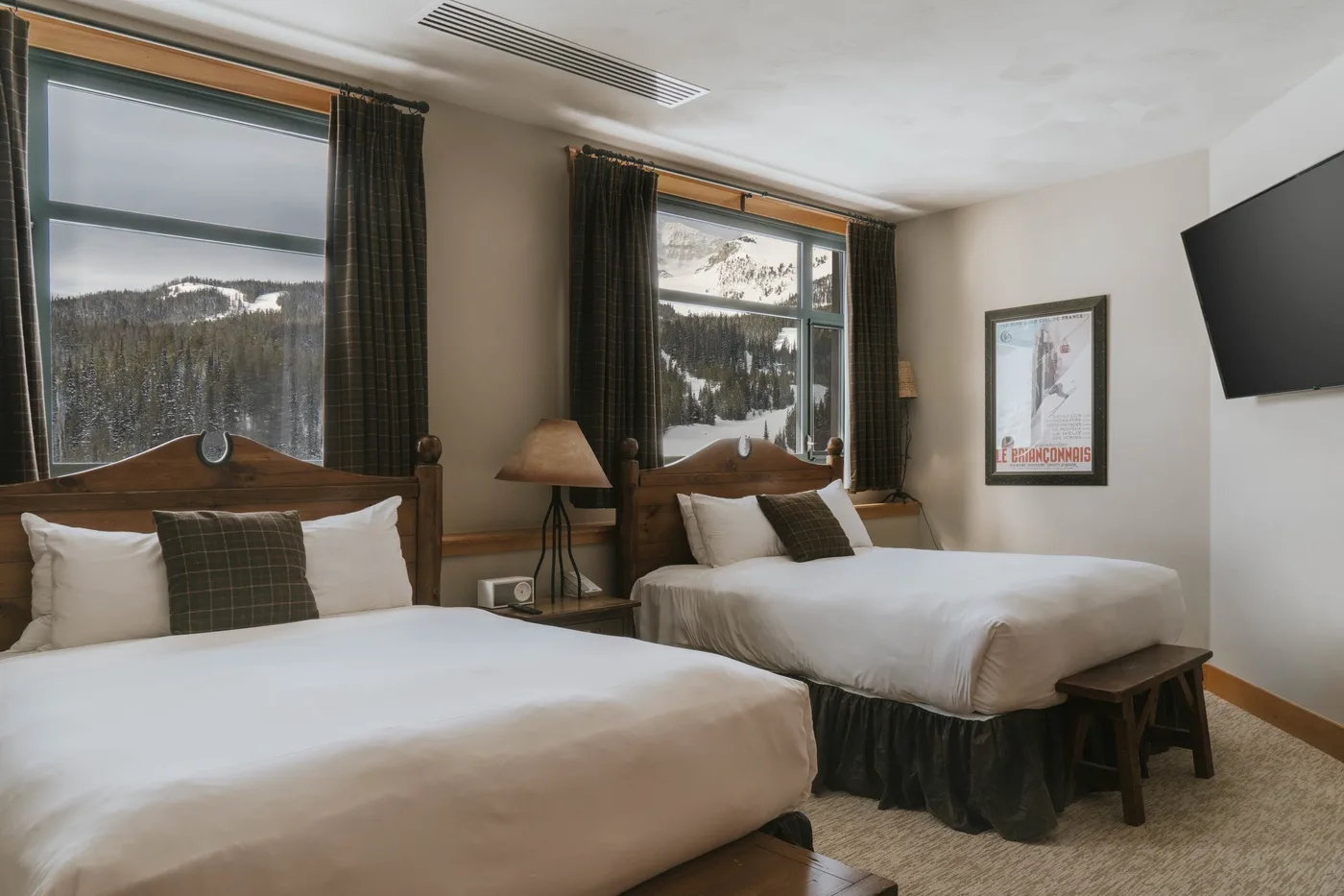 A bedroom with two beds, dark curtains, and mountain views through the windows.