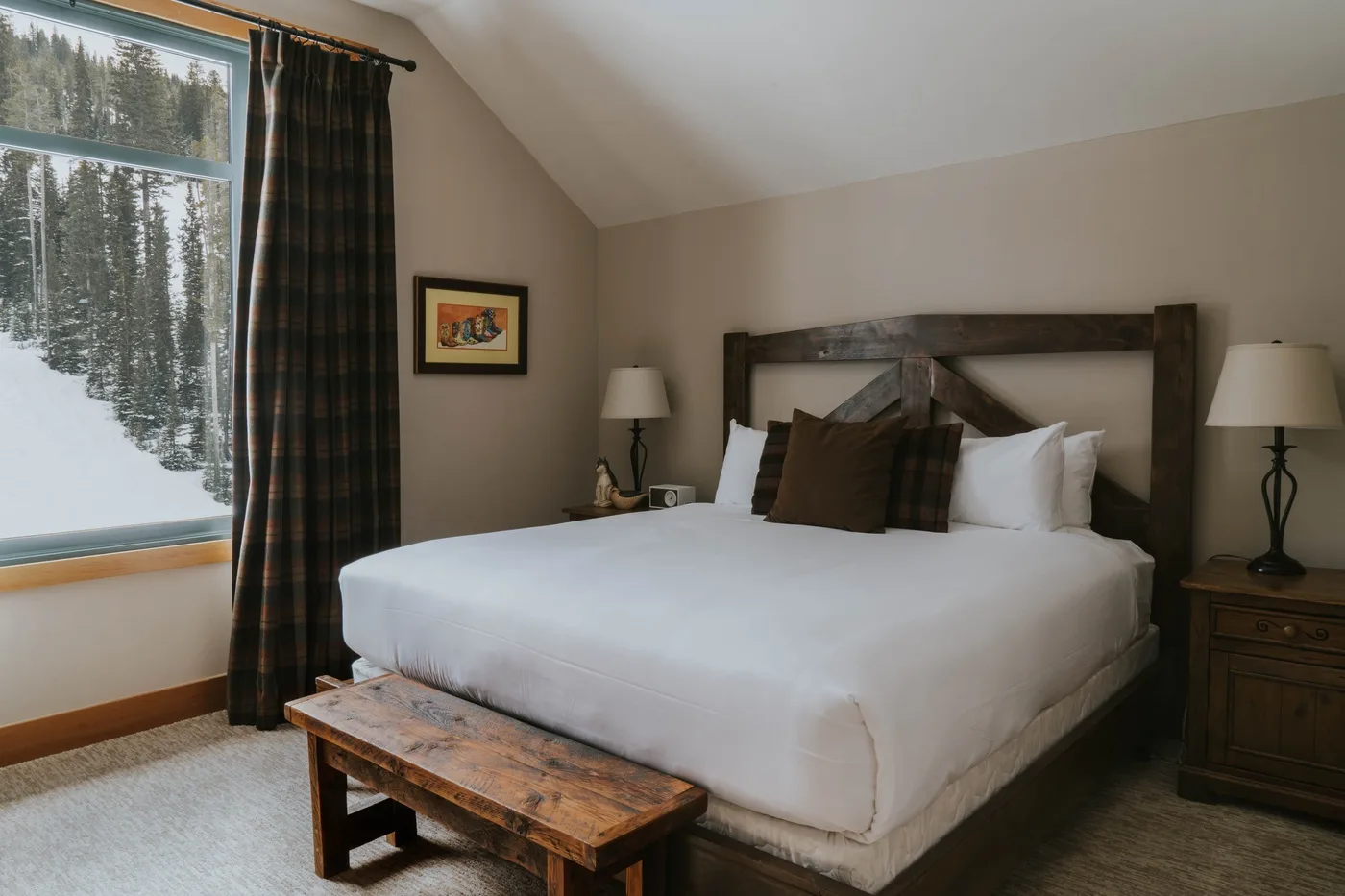 A bedroom with a large bed, bedside lamps, and a window overlooking snowy trees.