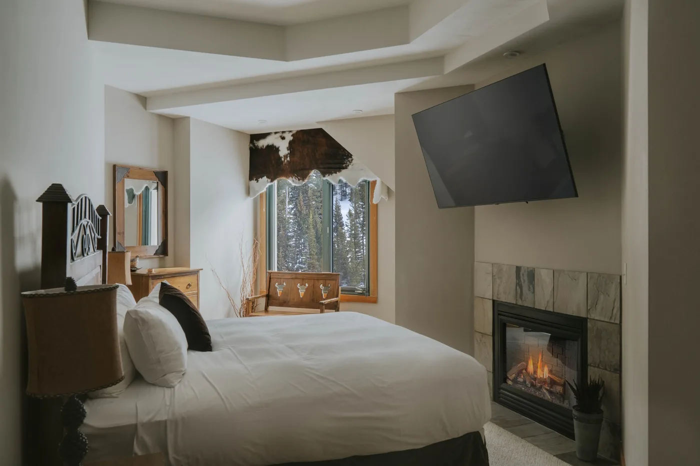 A bedroom with a large bed, a fireplace, and a wall-mounted television.