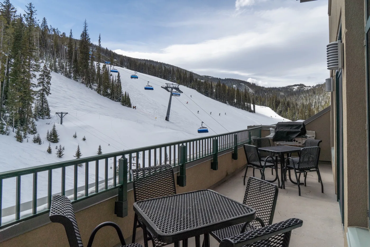 A patio with outdoor seating overlooks a snowy ski slope and chairlift.