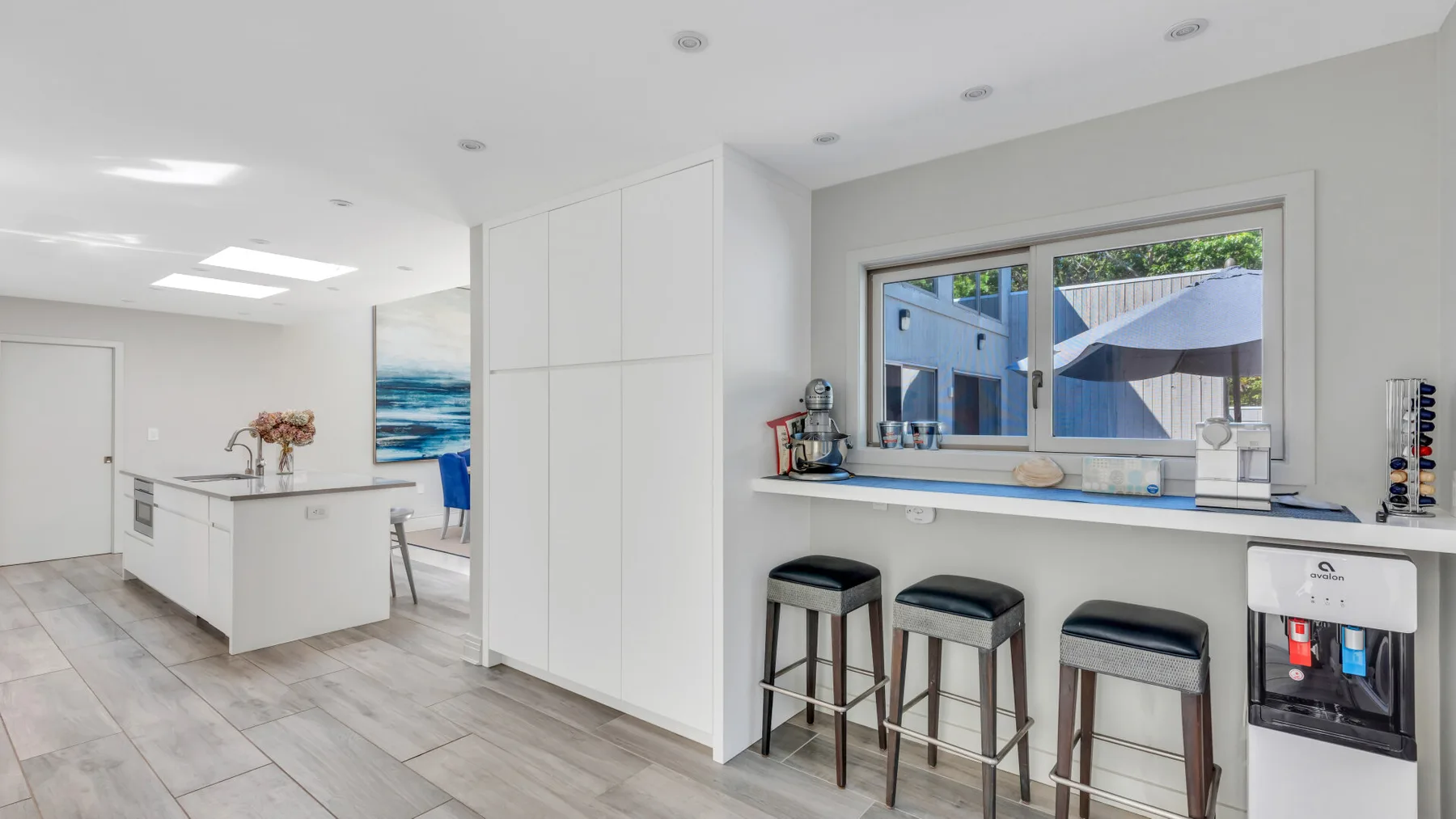 Una cocina luminosa con una isla blanca y una ventana amplia con vistas a un patio exterior.
