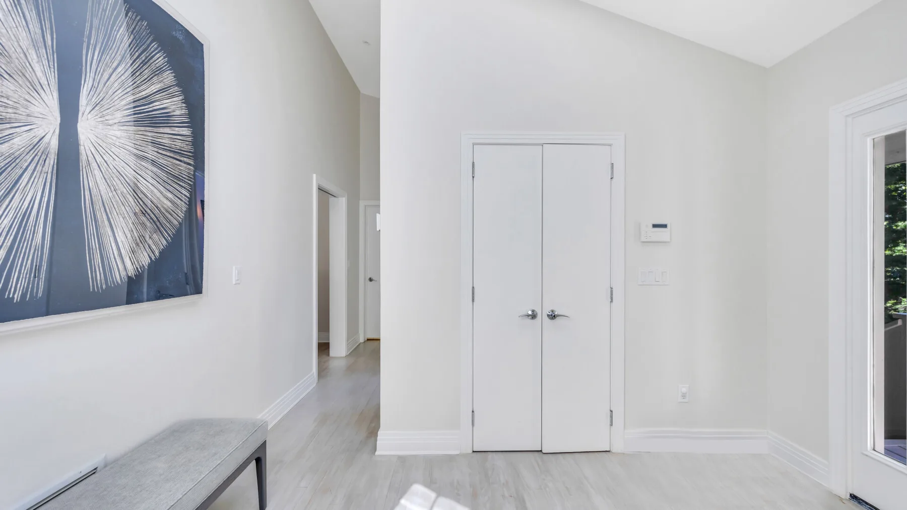 Un recibidor luminoso con puertas dobles blancas y una obra abstracta enmarcada.