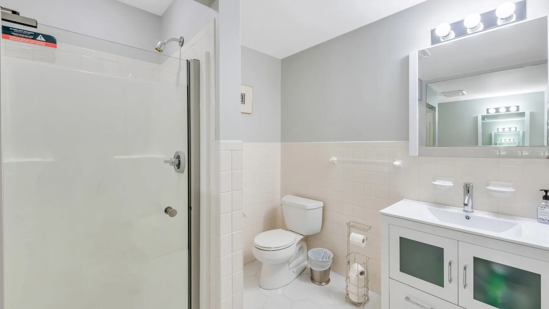 Un baño con inodoro, ducha y lavabo bajo un espejo grande.