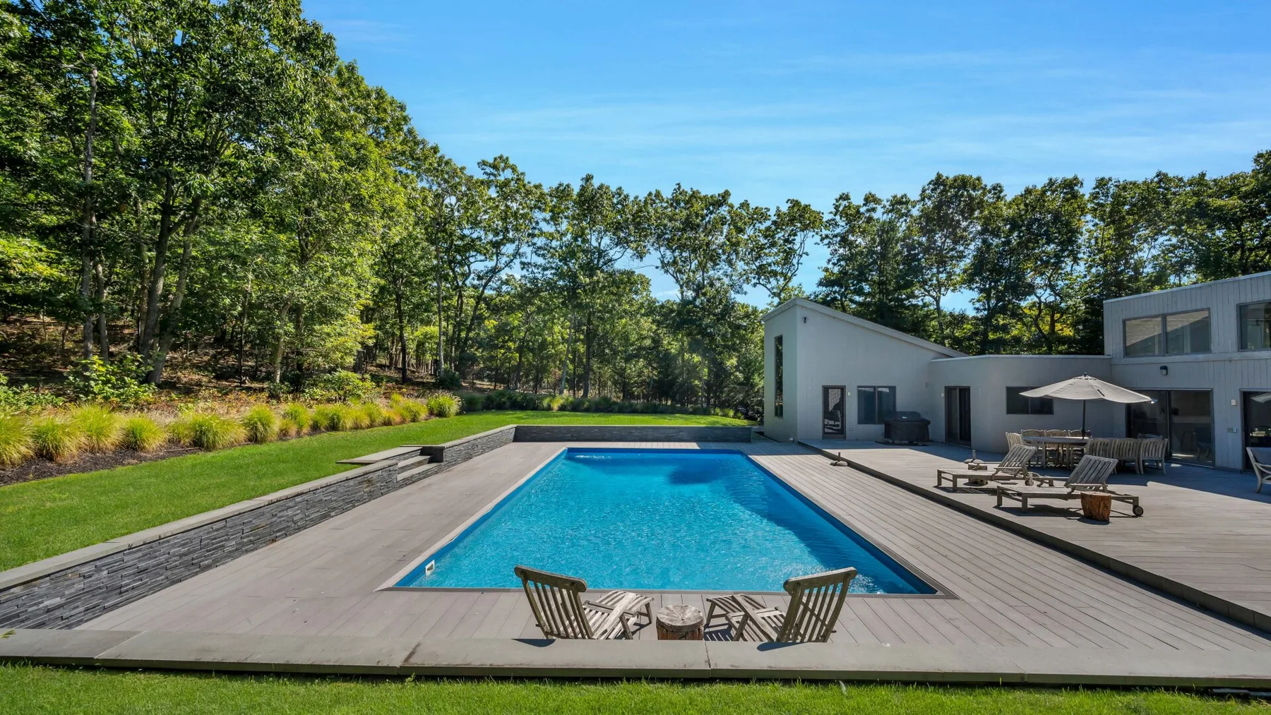 Una piscina al aire libre está junto a una casa moderna, rodeada de árboles.
