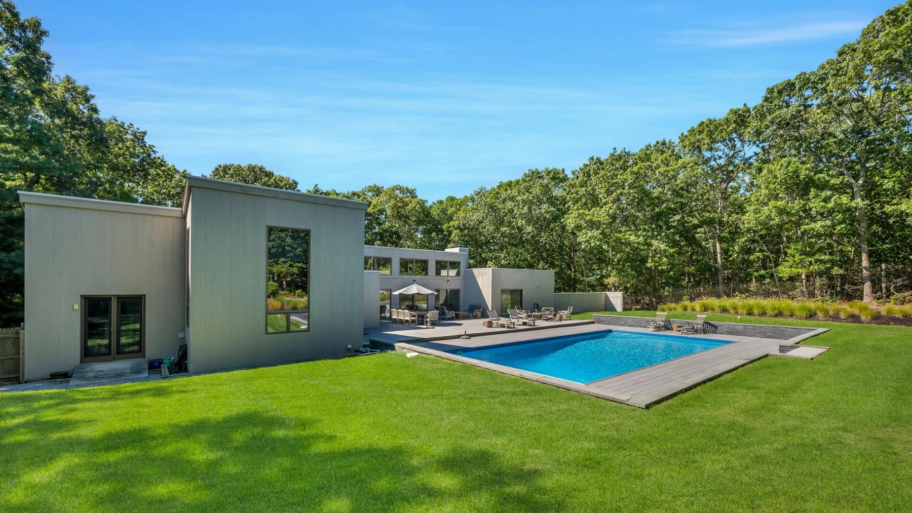 Una casa moderna junto a una piscina, con un amplio césped verde.