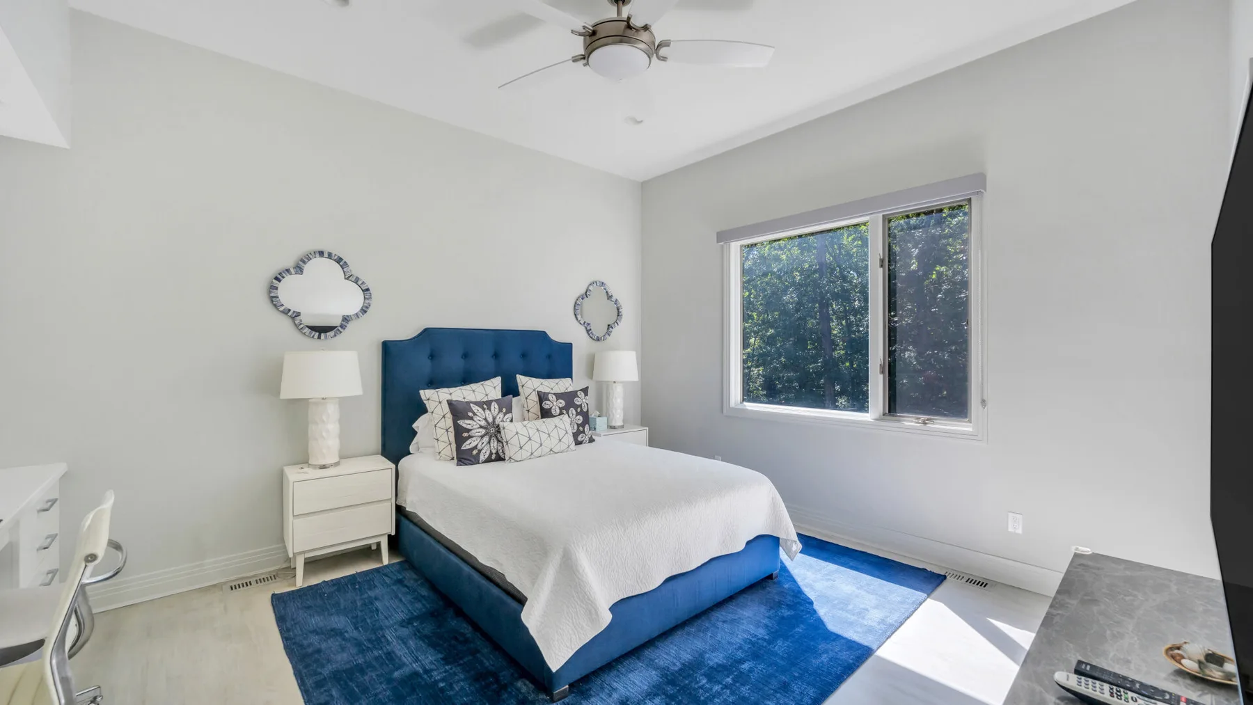 Un dormitorio luminoso con una cama azul, ropa de cama blanca y una ventana amplia.