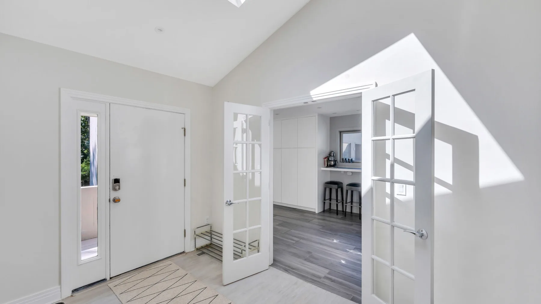 Una entrada luminosa se abre a una cocina a través de puertas con paneles de vidrio.