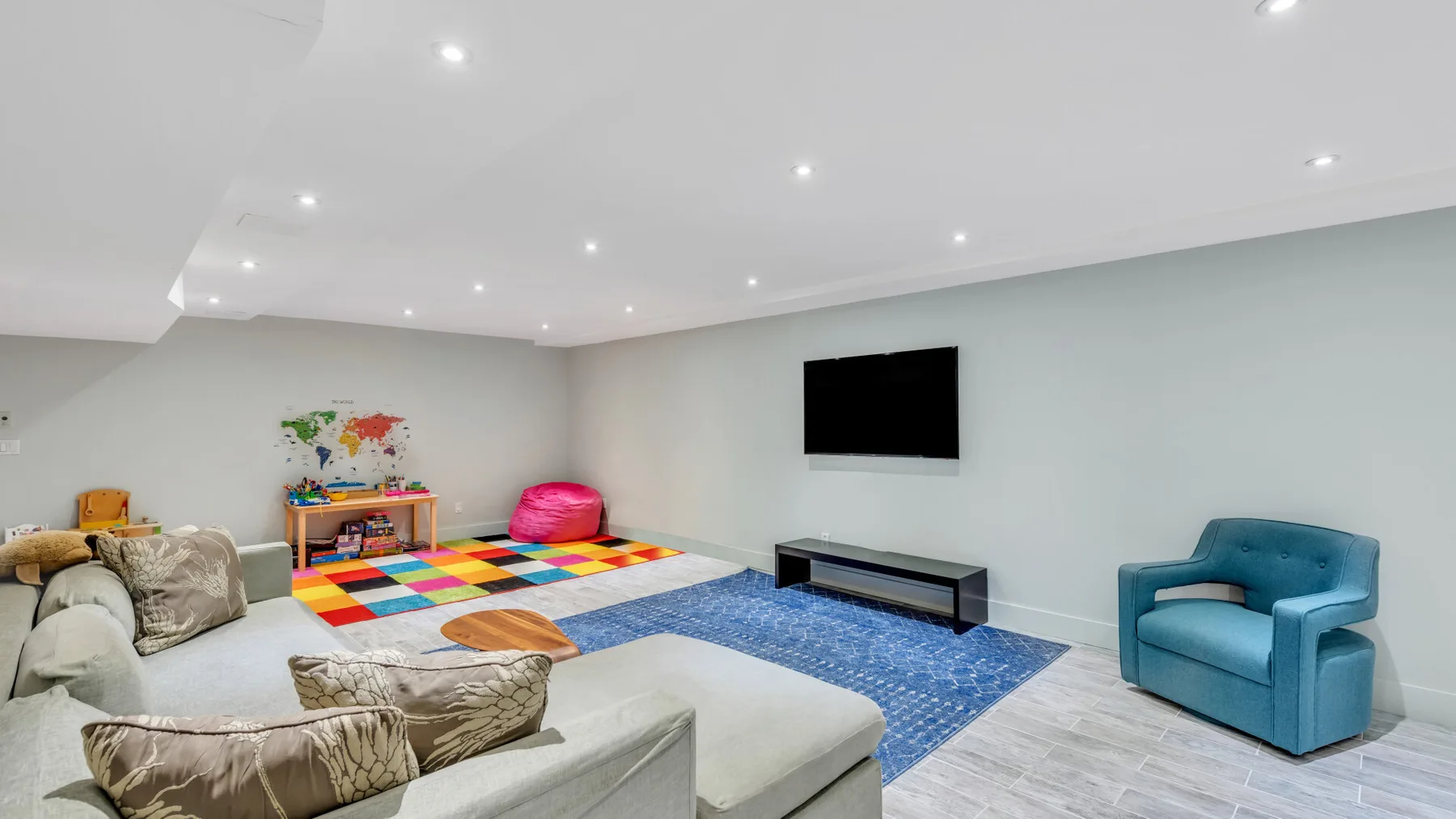 Una sala de juegos con tapetes coloridos, asientos y un televisor en la pared.