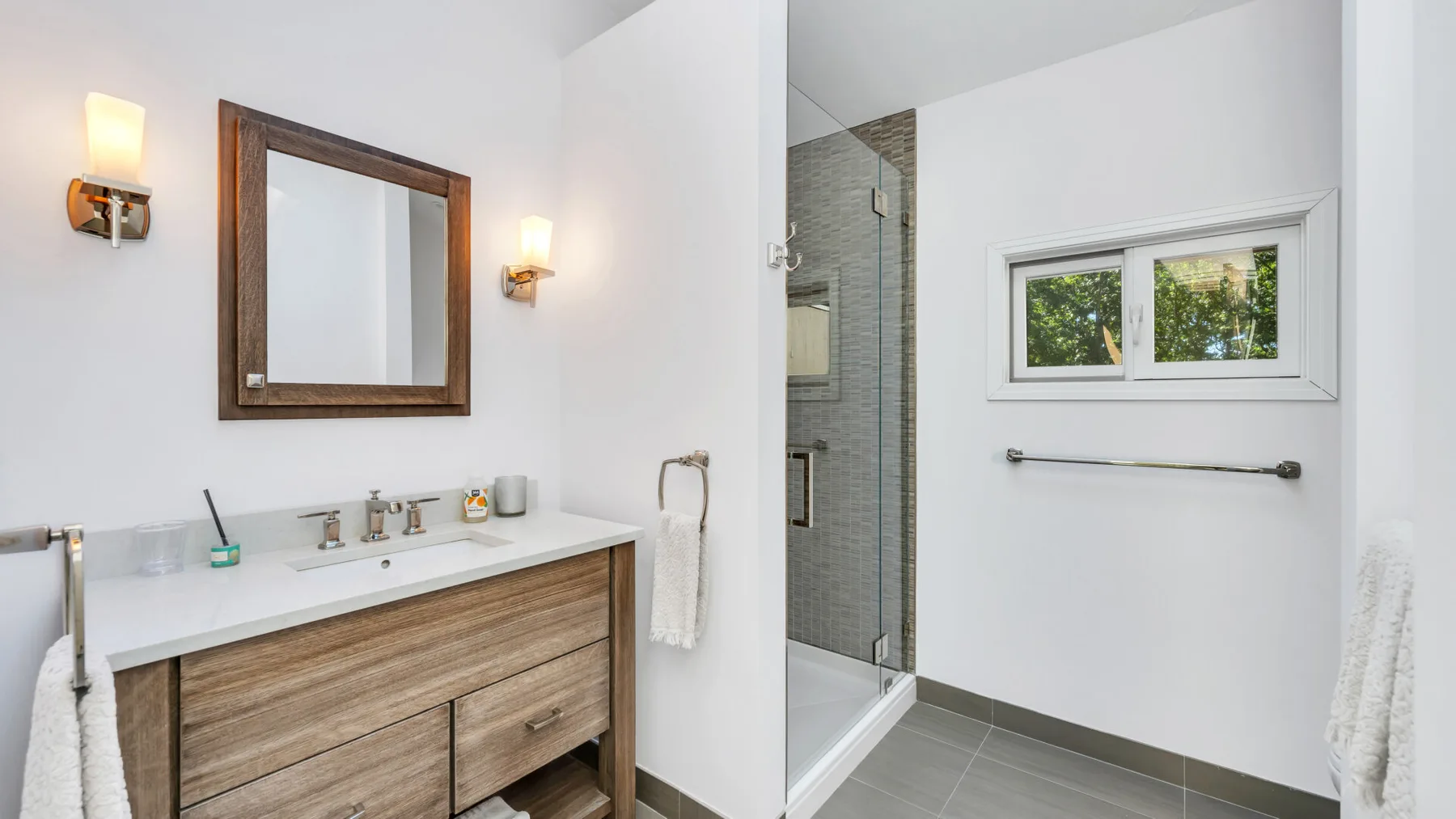 Un baño luminoso con lavabo, espejo de pared y ducha de vidrio.