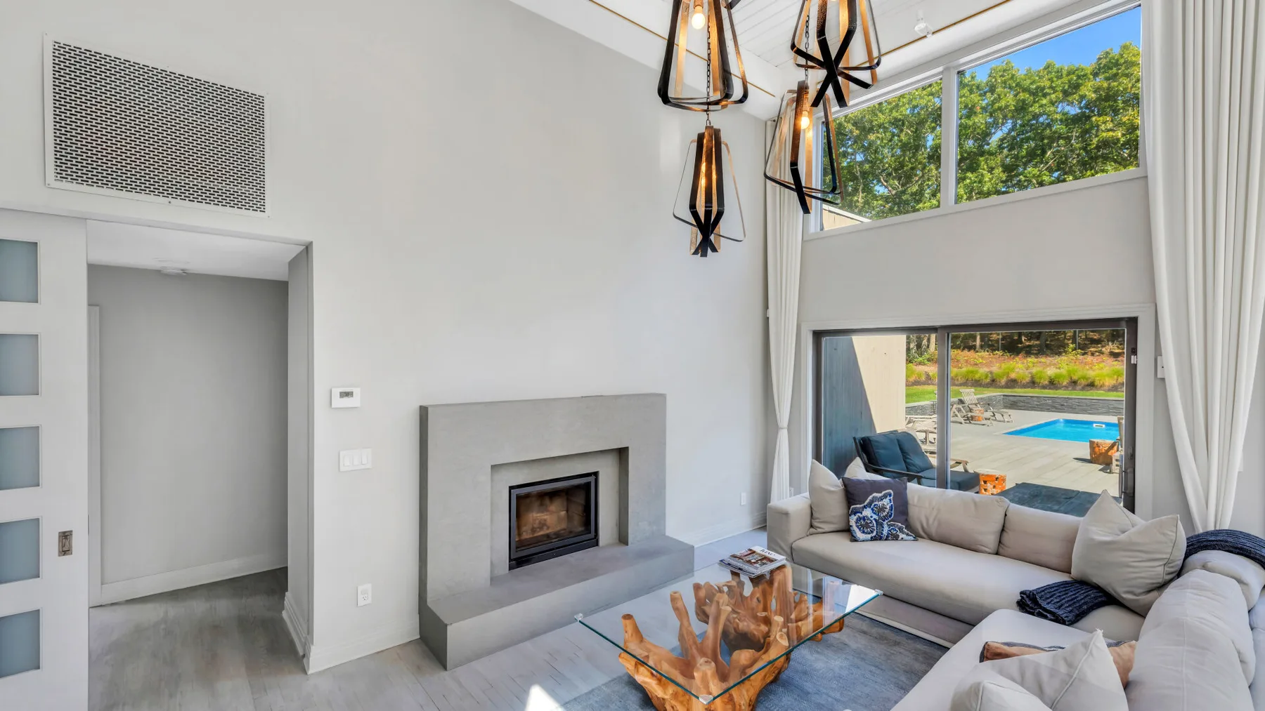 Una sala luminosa con chimenea, asientos y grandes ventanas con vistas a una piscina.