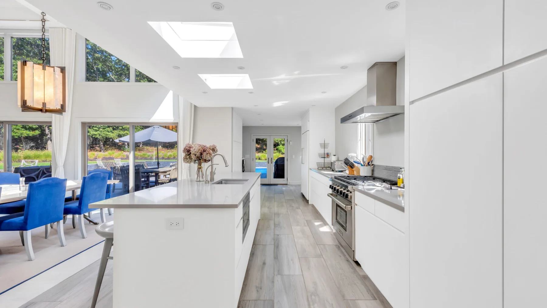Una cocina abierta y luminosa cuenta con una isla larga y armarios blancos.