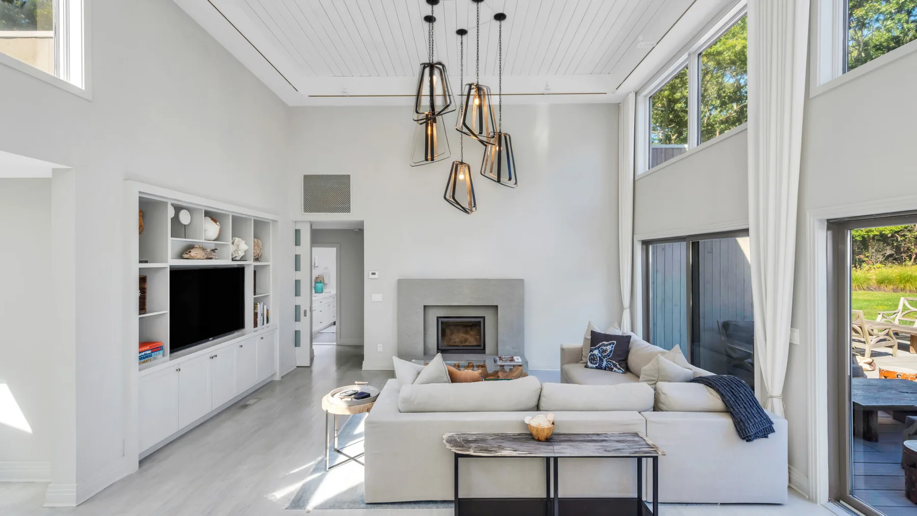 Una sala luminosa con chimenea, asientos blancos y ventanas grandes.