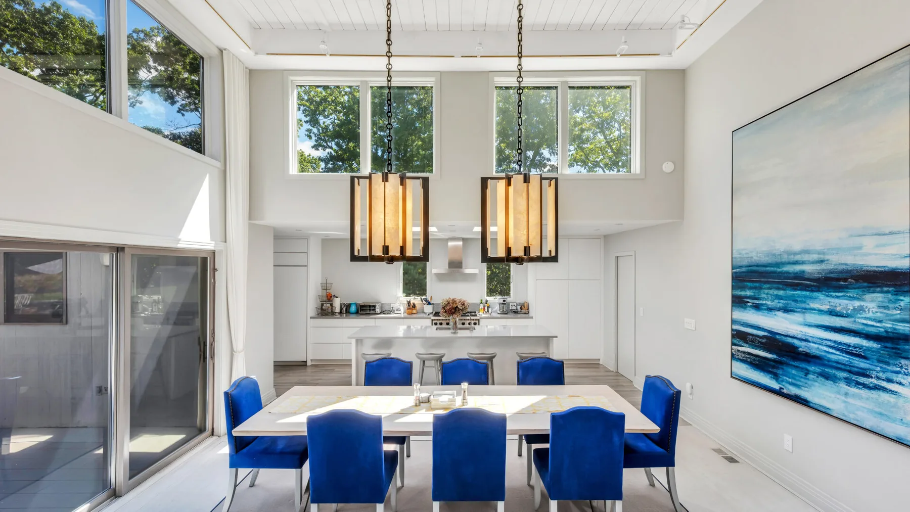 Un comedor luminoso con asientos azules, una mesa larga y ventanas grandes.