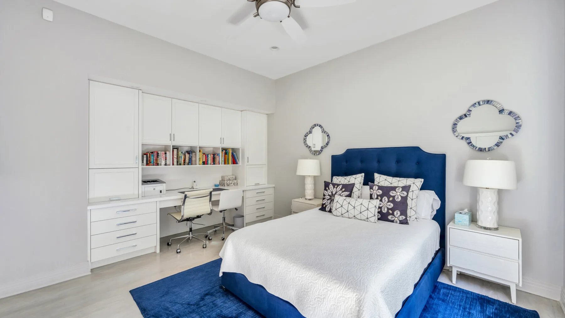 Un dormitorio luminoso con una cama azul, ropa de cama blanca y un escritorio empotrado.
