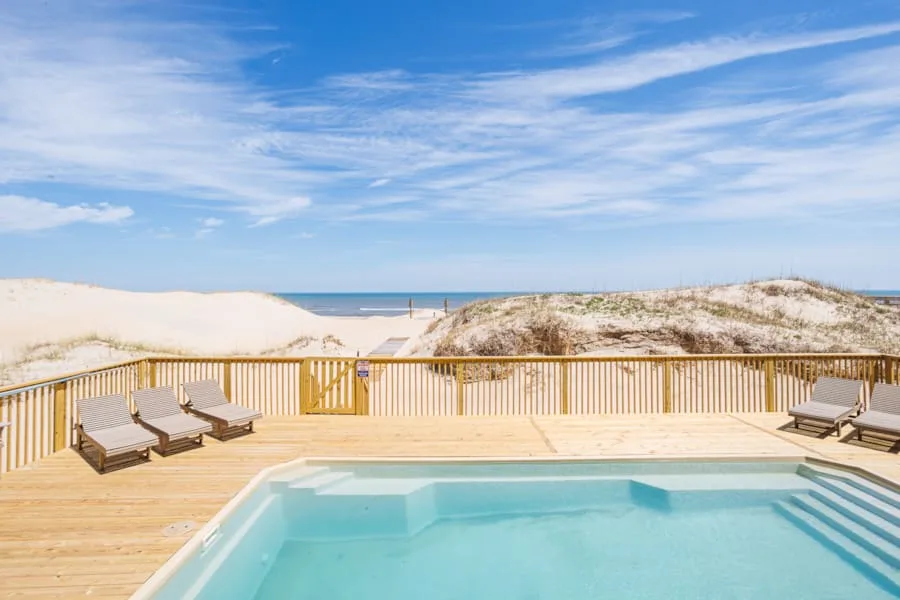 A swimming pool and lounge seating overlook sandy dunes and the ocean.