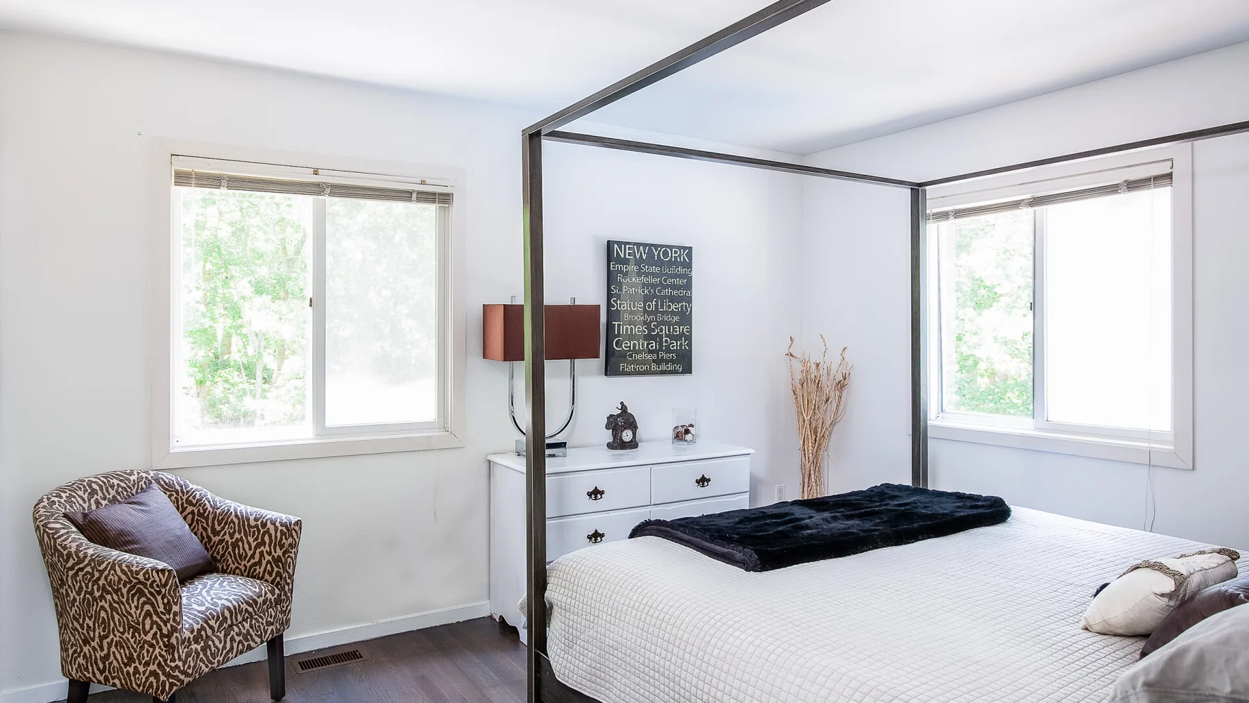 Un dormitorio luminoso con una cama con dosel, una cómoda y ventanas.