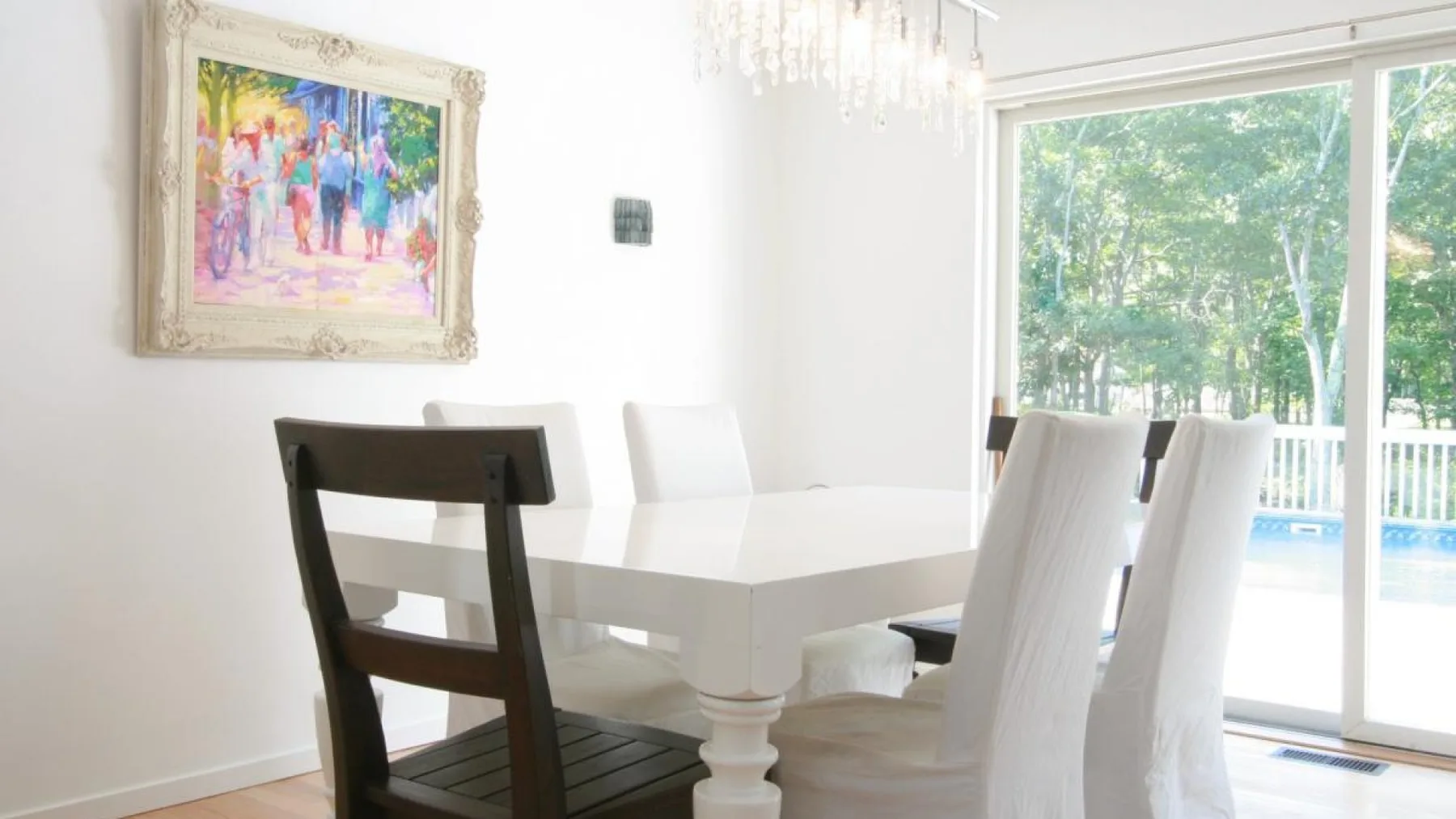Un comedor luminoso tiene una mesa blanca y sillas junto a grandes ventanas.