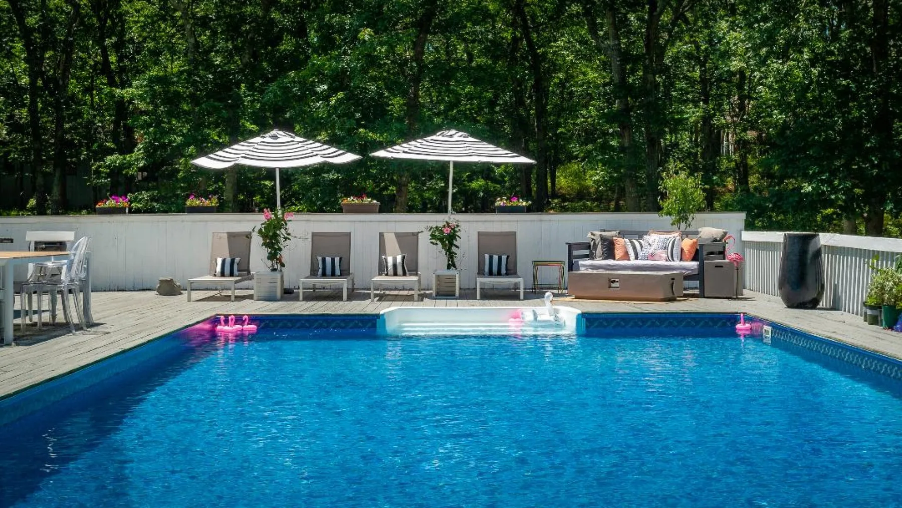 Una piscina al aire libre está junto a una terraza con asientos y sombrillas.