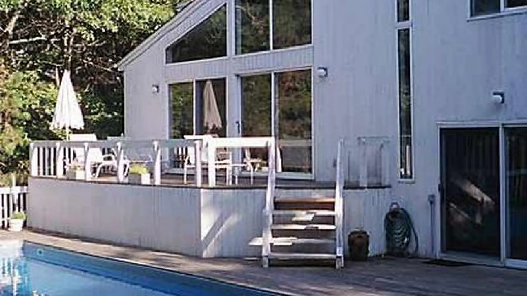 Una casa moderna da a una terraza de madera junto a una piscina.