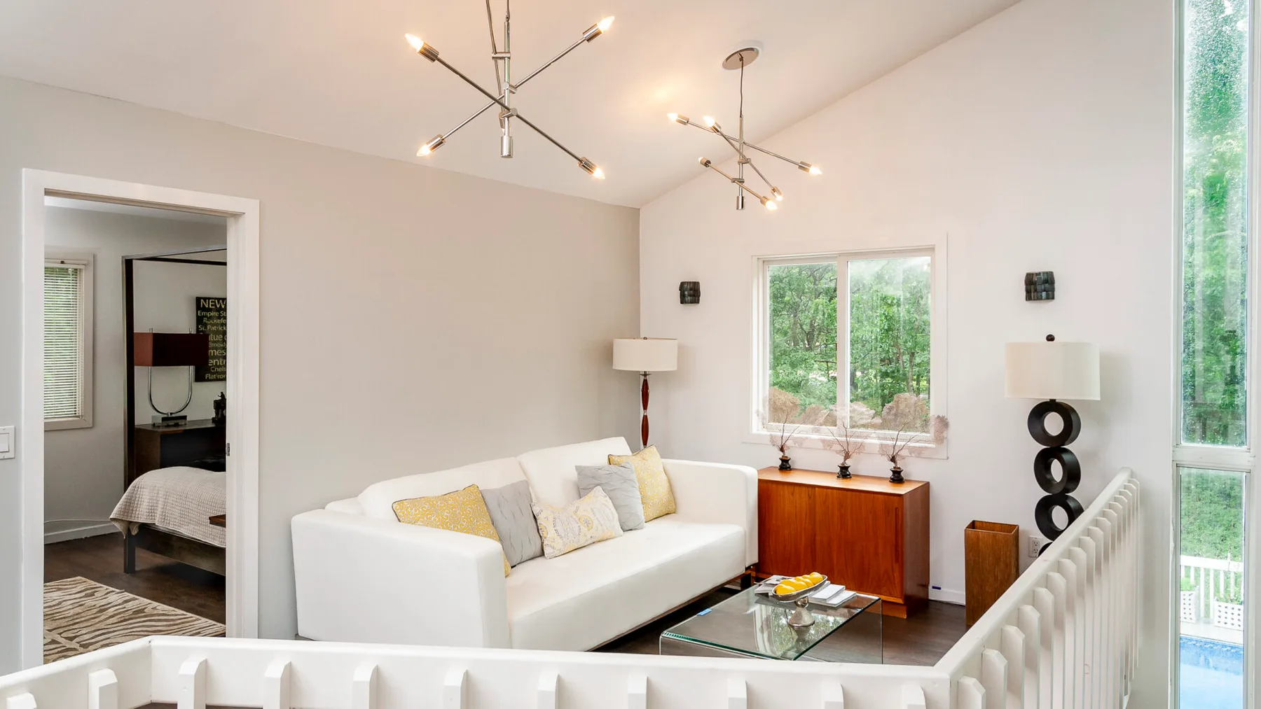 A bright living room with white seating, a glass coffee table, and large windows.