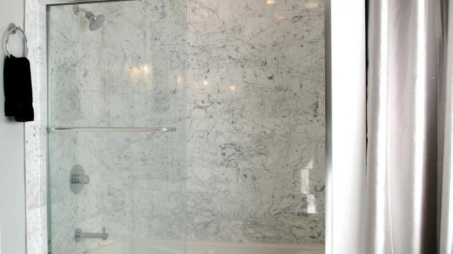 Una ducha de baño con paredes de patrón pétreo claro y un panel de vidrio.
