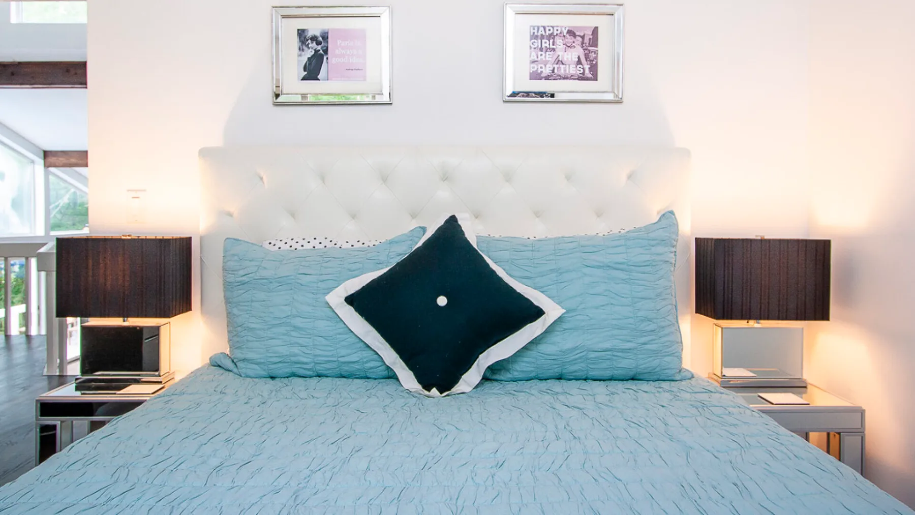 Un dormitorio con una cama vestida con ropa de cama azul claro y cojines oscuros.