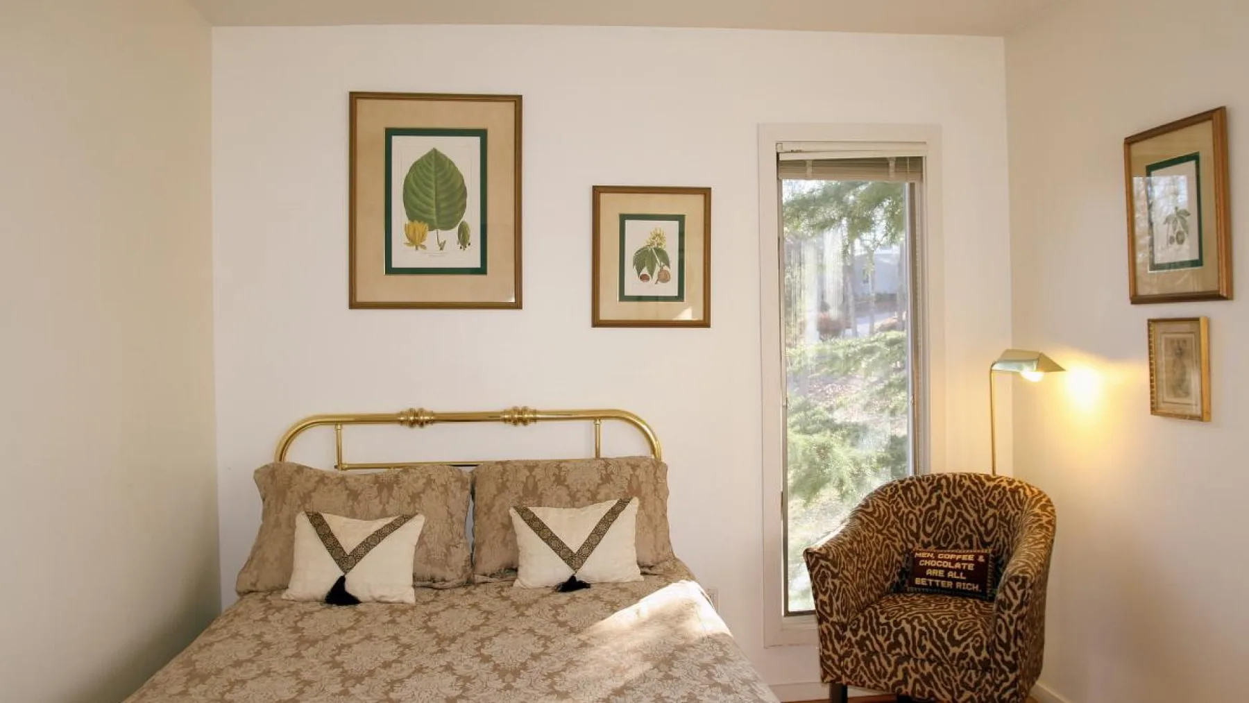 Un dormitorio con una cama, láminas botánicas enmarcadas y un sillón estampado.