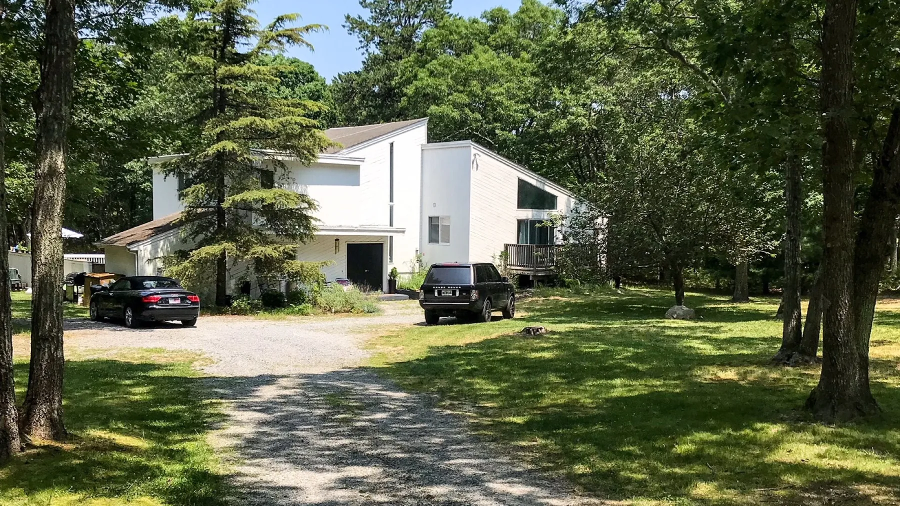 Una casa blanca moderna está entre árboles junto a un camino de grava.