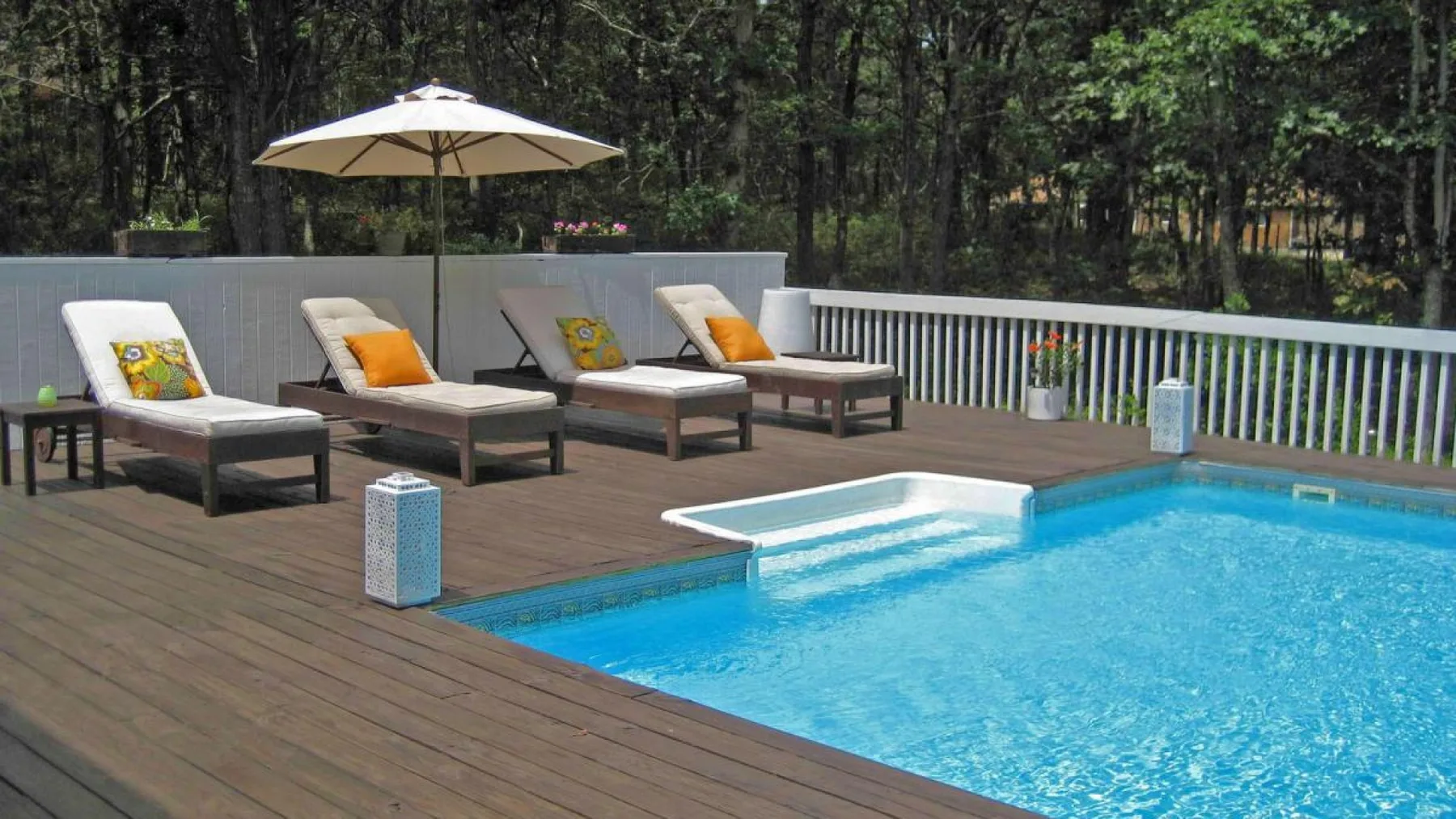 Una piscina al aire libre junto a una terraza de madera con asientos y una sombrilla.