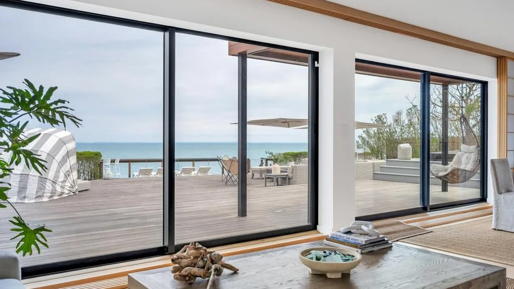 Una luminosa sala de estar da a una terraza de madera con vistas al mar.