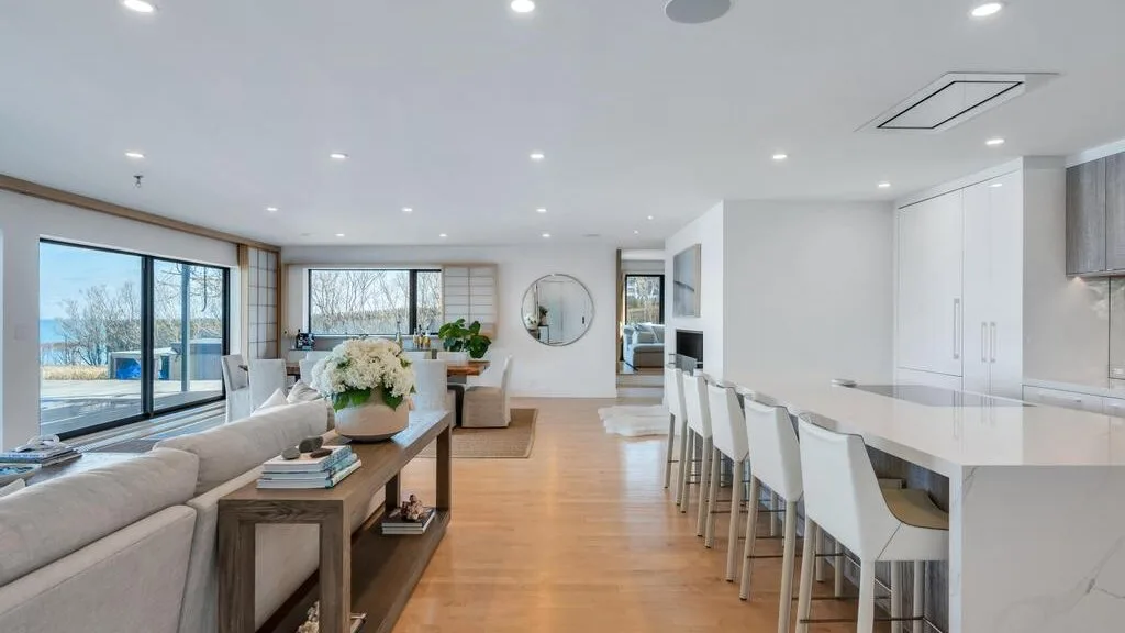 Una luminosa sala-comedor de planta abierta con una larga isla de cocina y grandes ventanas.