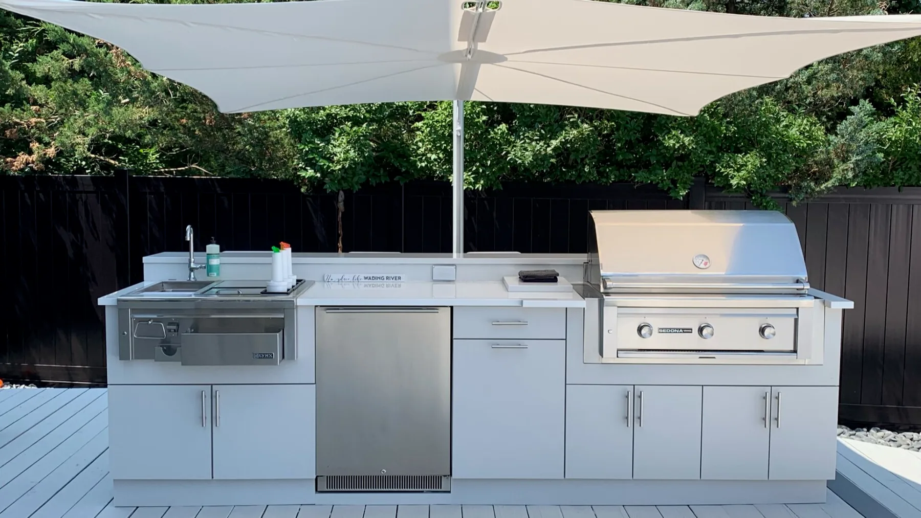 Una cocina exterior con una parrilla de acero inoxidable está bajo una gran sombrilla.