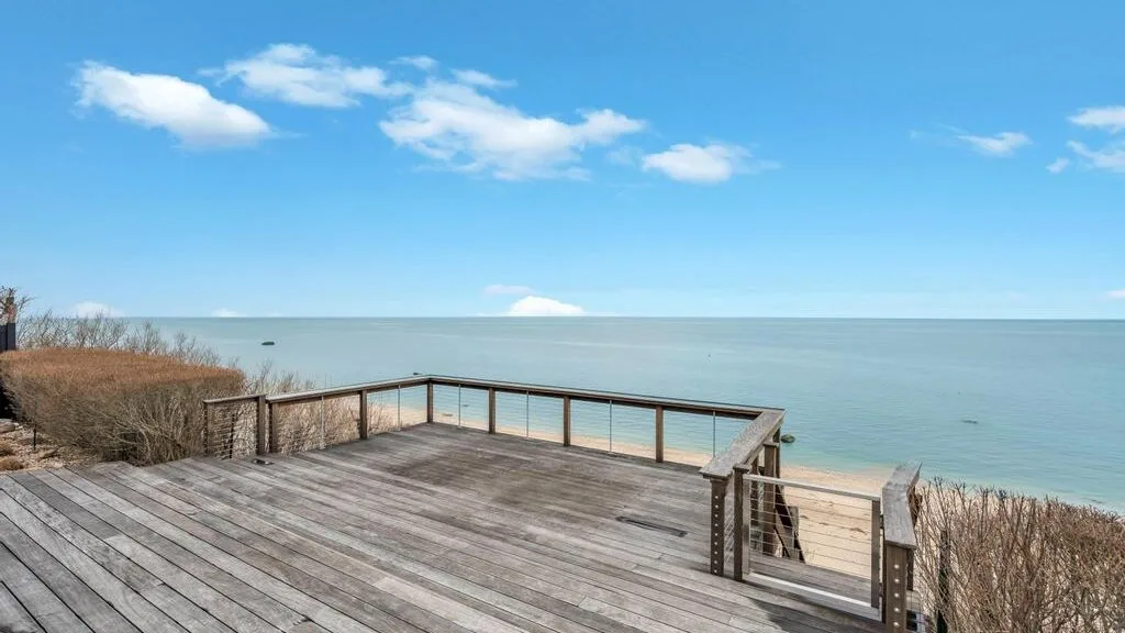 Una terraza de madera da a aguas tranquilas bajo un cielo azul despejado.
