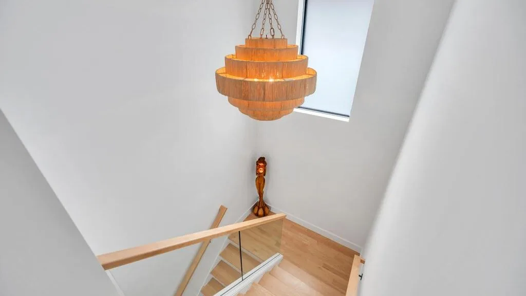 Una escalera luminosa con una barandilla de madera y una lámpara colgante.