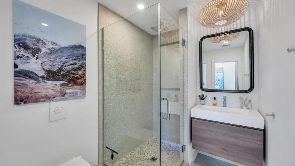 Un baño moderno con una ducha de vidrio y un tocador bajo un espejo.