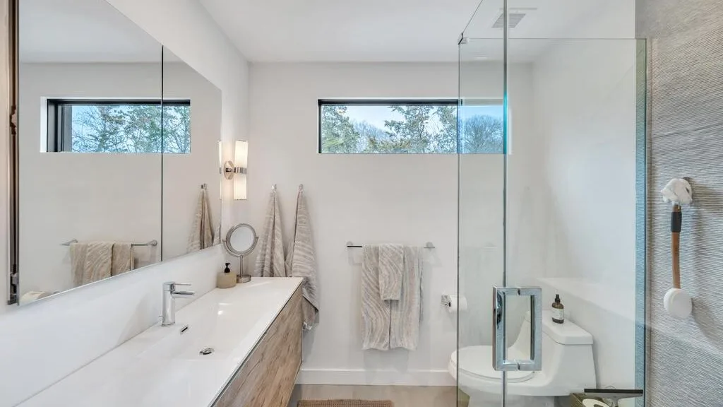 Un baño luminoso con un lavabo largo, espejo y ducha de cristal.
