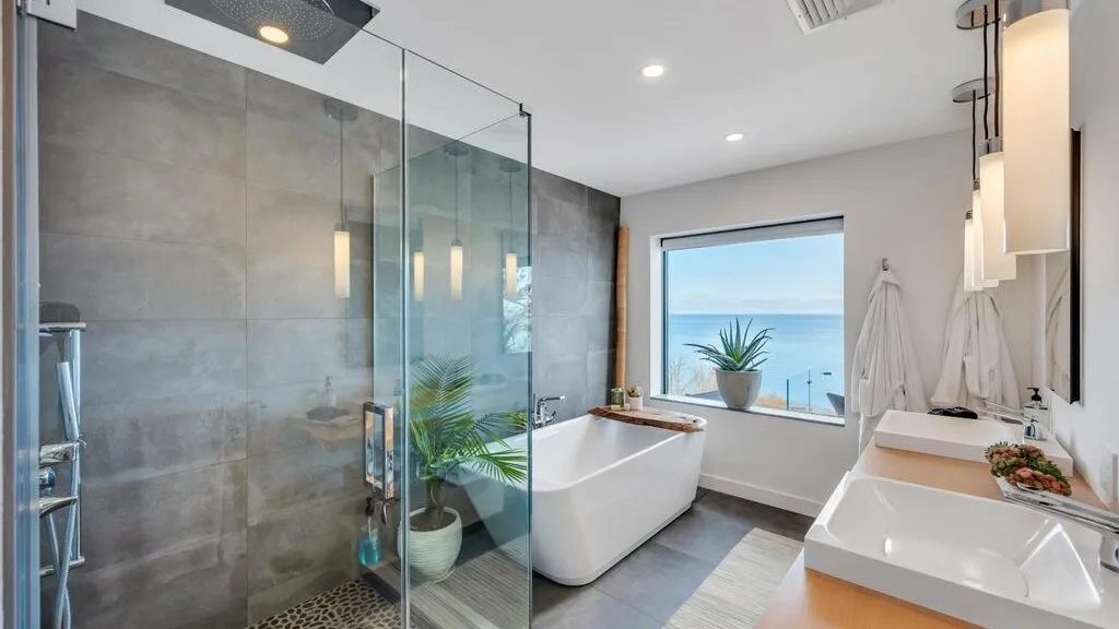 Un baño moderno con bañera exenta, ducha de vidrio y ventana con vista al agua.