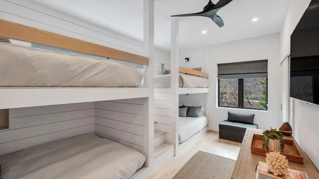 Un dormitorio luminoso con literas, un pequeño sofá y una ventana.