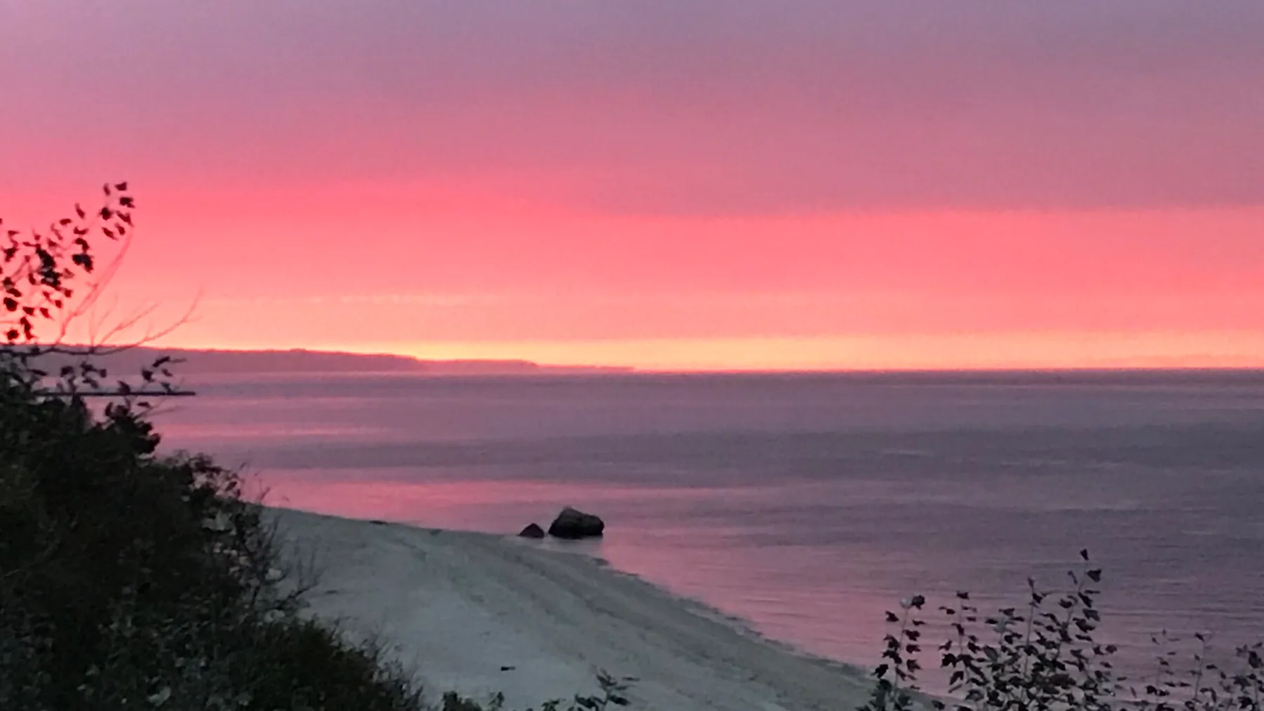 Un atardecer rosado ilumina el océano, con una orilla oscura en primer plano.