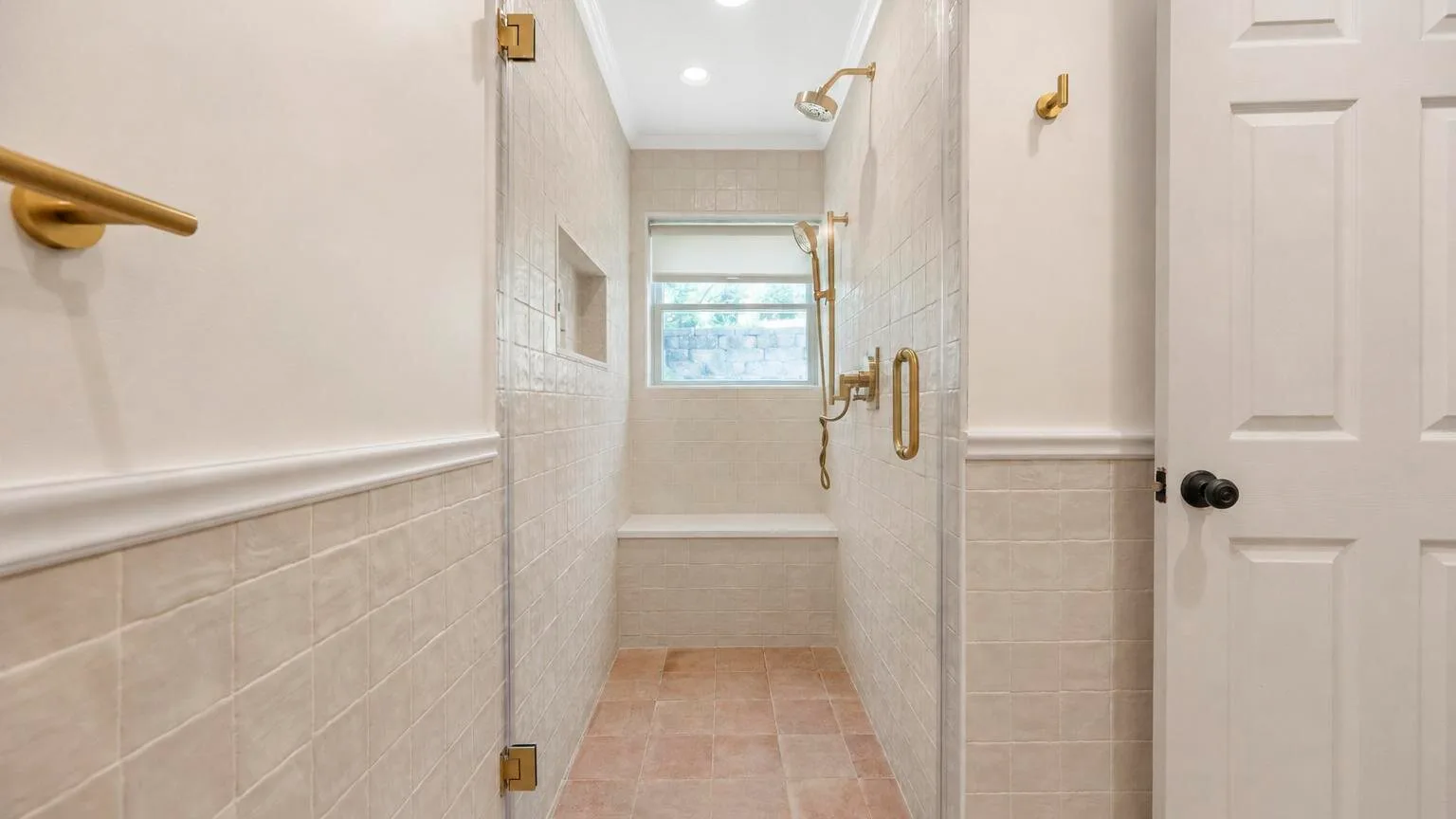 Un baño con azulejos, una zona de ducha y una ventana al fondo.