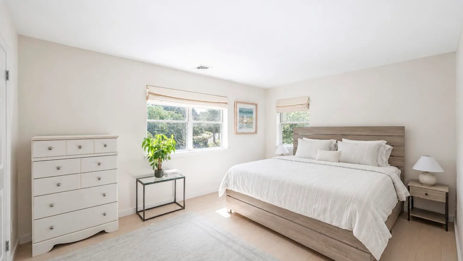 Un dormitorio luminoso con una cama, una cómoda y ventanas.