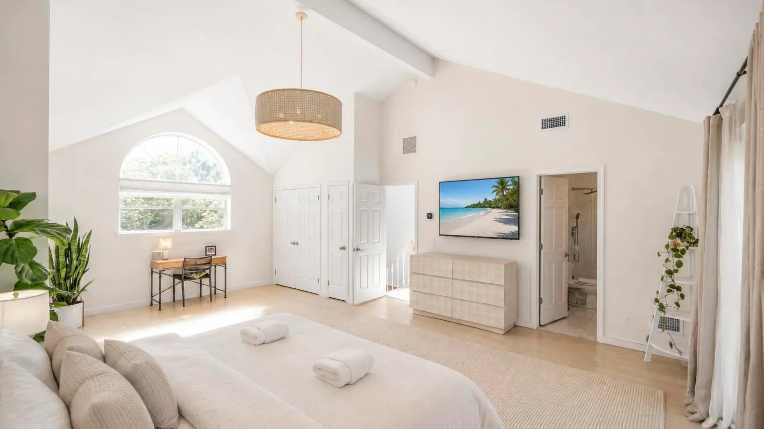 Un dormitorio luminoso con una cama, una cómoda y una gran ventana arqueada.